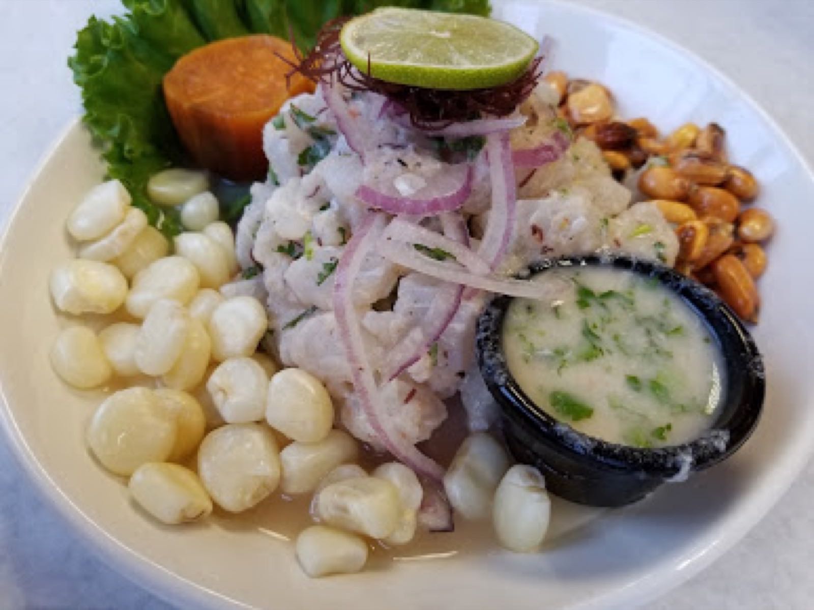 Classic ceviche with red onion, choclo and sweet potato on a white plate